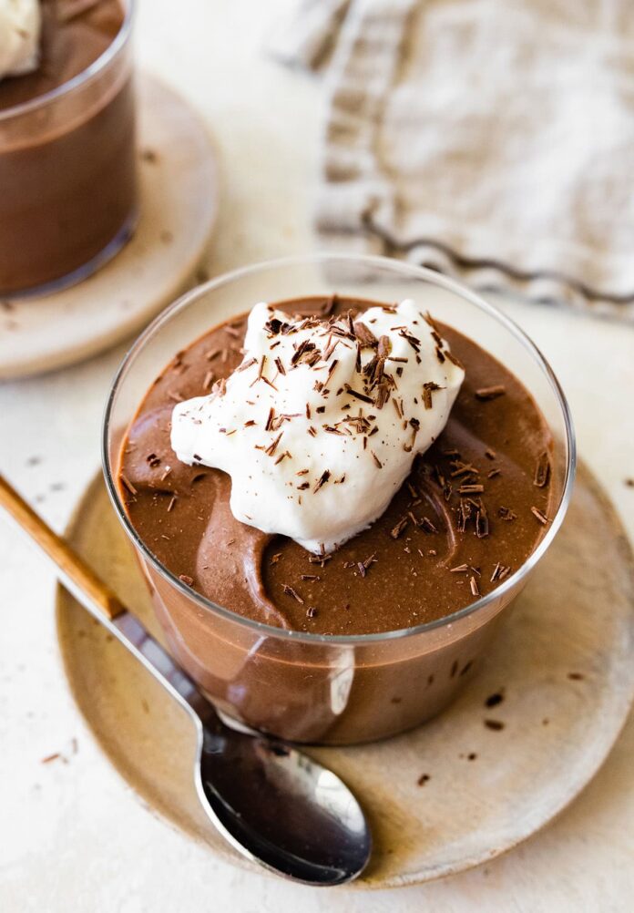 A hard boiled egg chocolate pudding in a glass container, topped with whipped cream and chocolate shavings.