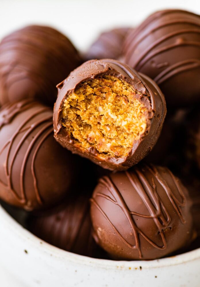 Chocolate covered peanut butter balls in a bowl with one ball having a bite taken from it.