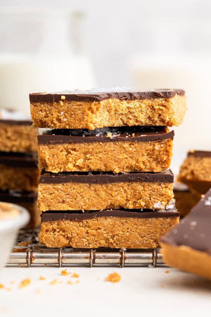 Four peanut butter bars stacked on top of each other on a wire cooling rack. The top bar has a bite taken out of it.