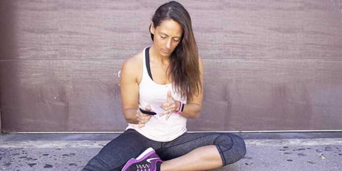 A woman sitting on the ground checking her blood sugar level