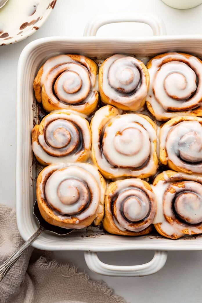 A white square baking dish filled with 9 baked cinnamon rolls that are topped with a glaze.