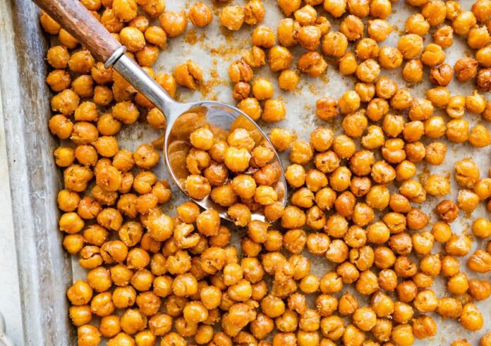 Spoon scooping crispy roasted chickpeas from a baking sheet.