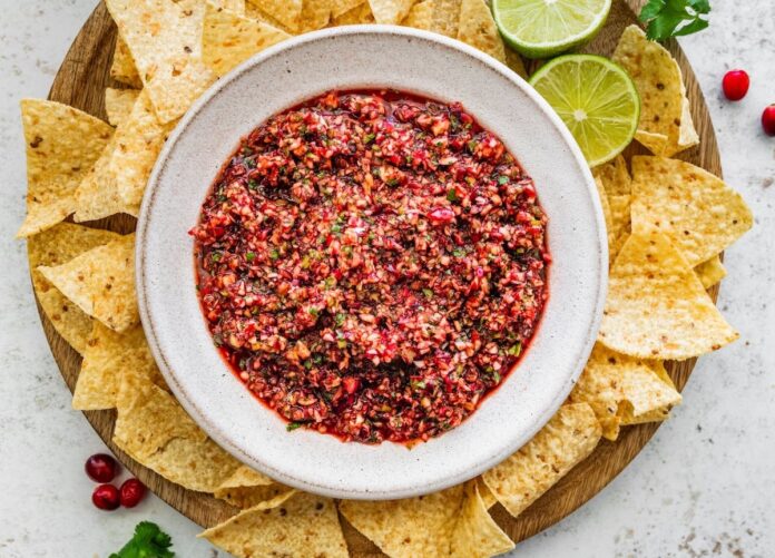Bowl of cranberry salsa surrounded by tortilla chips and lime wedges, ready to serve.